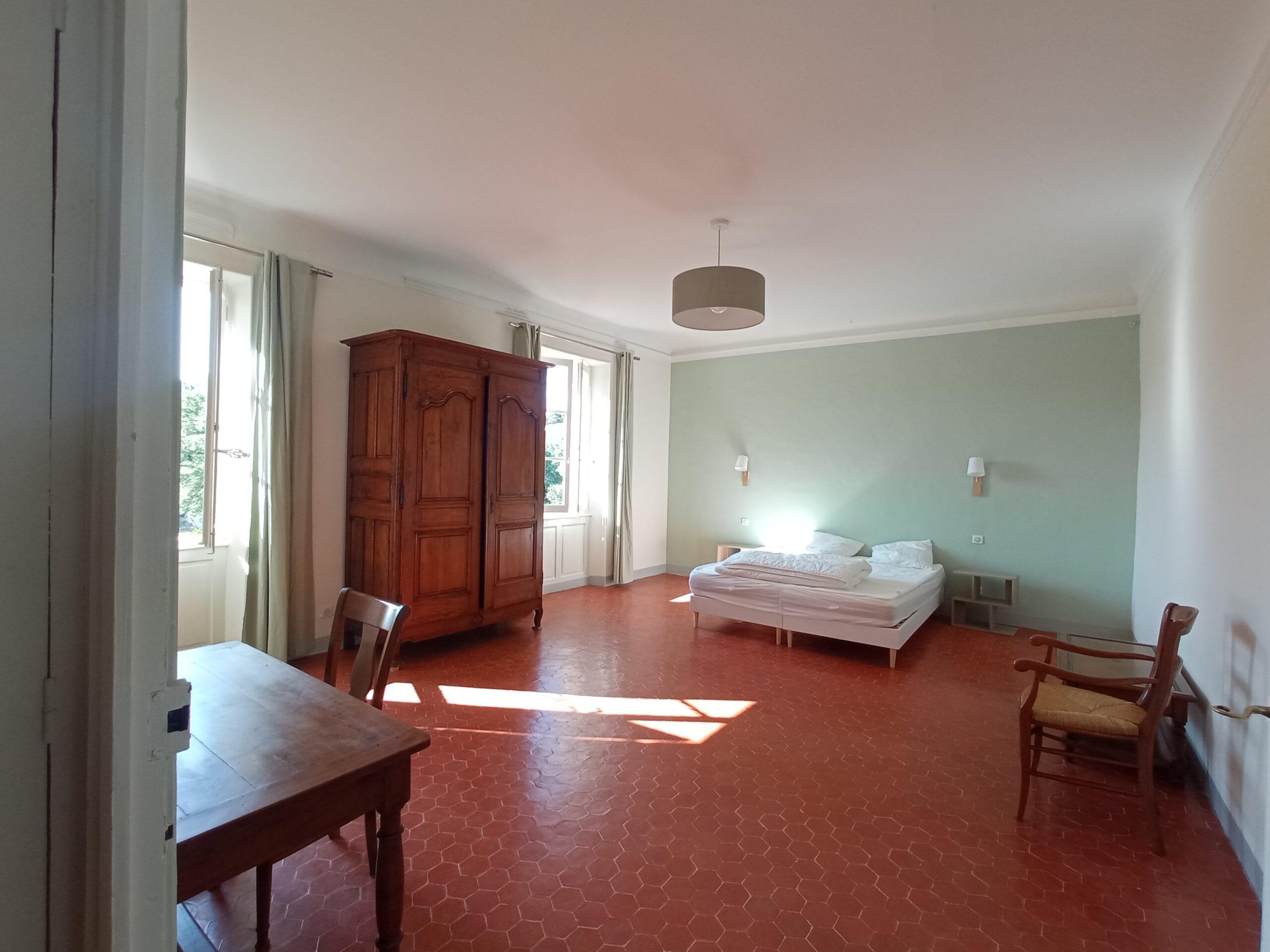 Intérieur spacieux de la chambre 6 dans la bastide du Domaine de Ribbe, avec son sol en tomettes, son lit double, son armoire ancienne en bois et sa décoration aux tons doux.