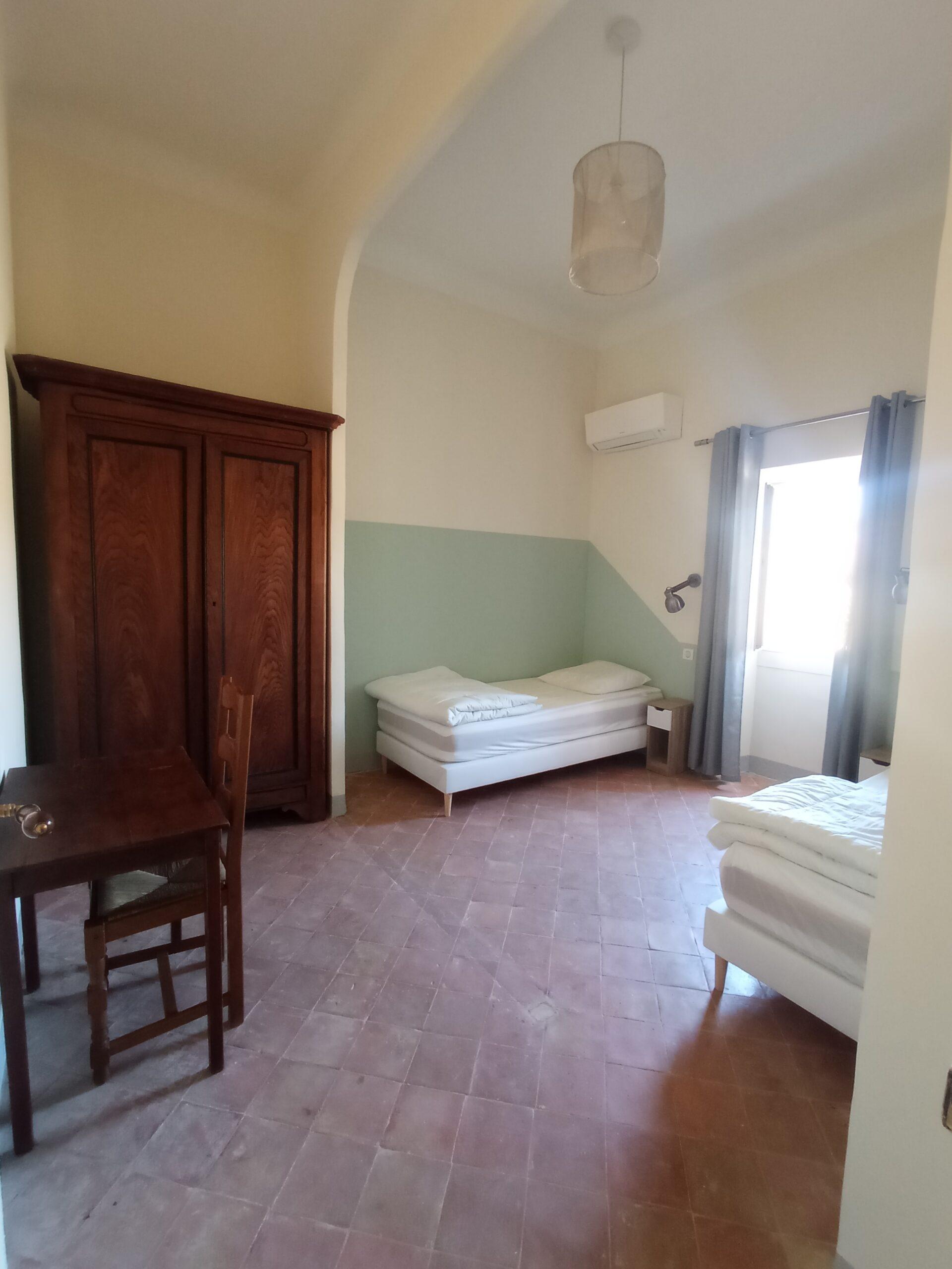 Vue intérieure de la chambre 8 dans la bastide du Domaine de Ribbe, avec deux lits simples, une armoire ancienne en bois et un sol en tomettes traditionnelles.