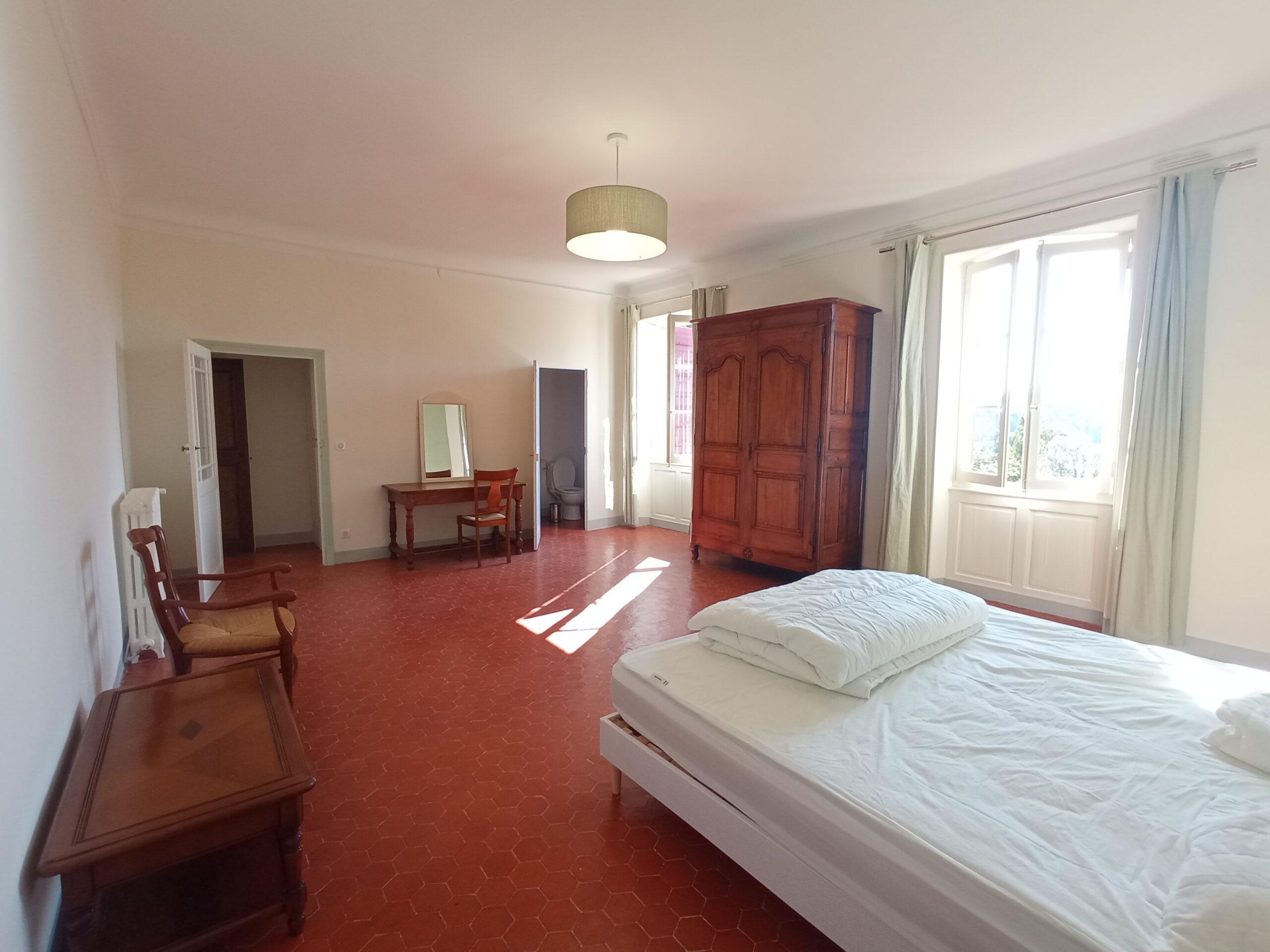Intérieur spacieux de la chambre 6 dans la bastide du Domaine de Ribbe, avec son sol en tomettes, son lit double, son armoire ancienne en bois et sa décoration aux tons doux.