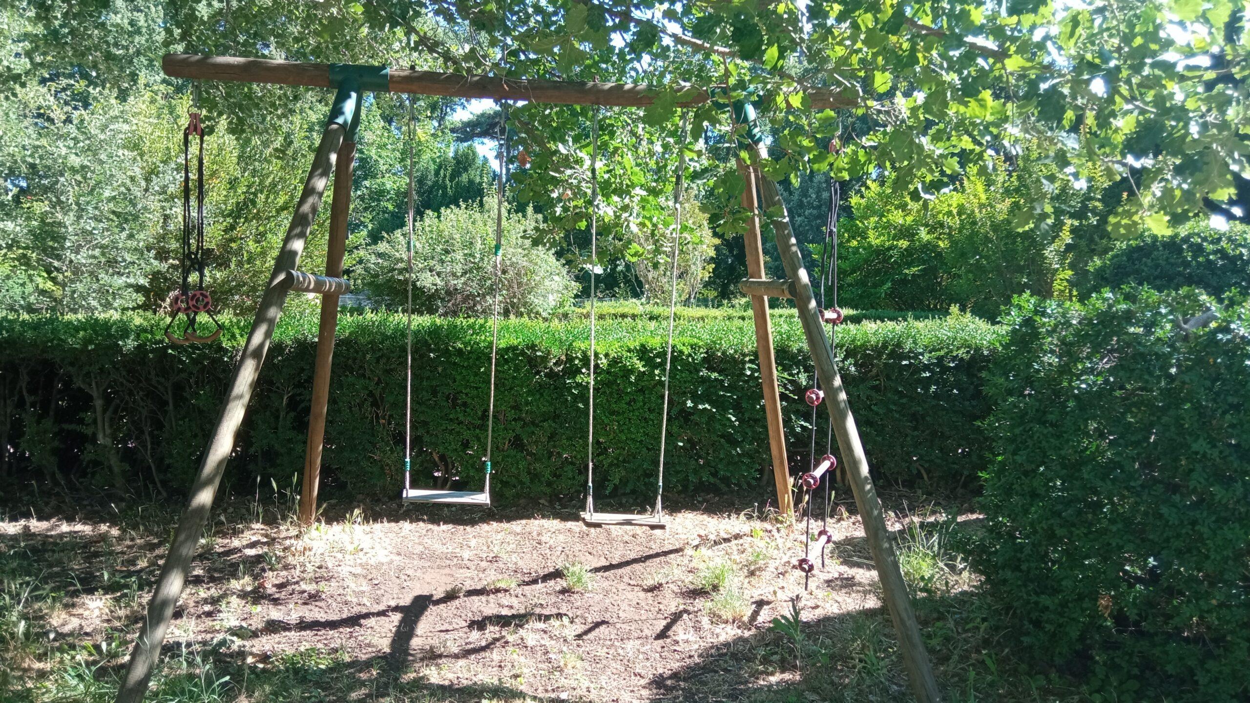 Aire de jeux extérieure en bois avec balançoires dans le grand jardin du Domaine de Ribbe