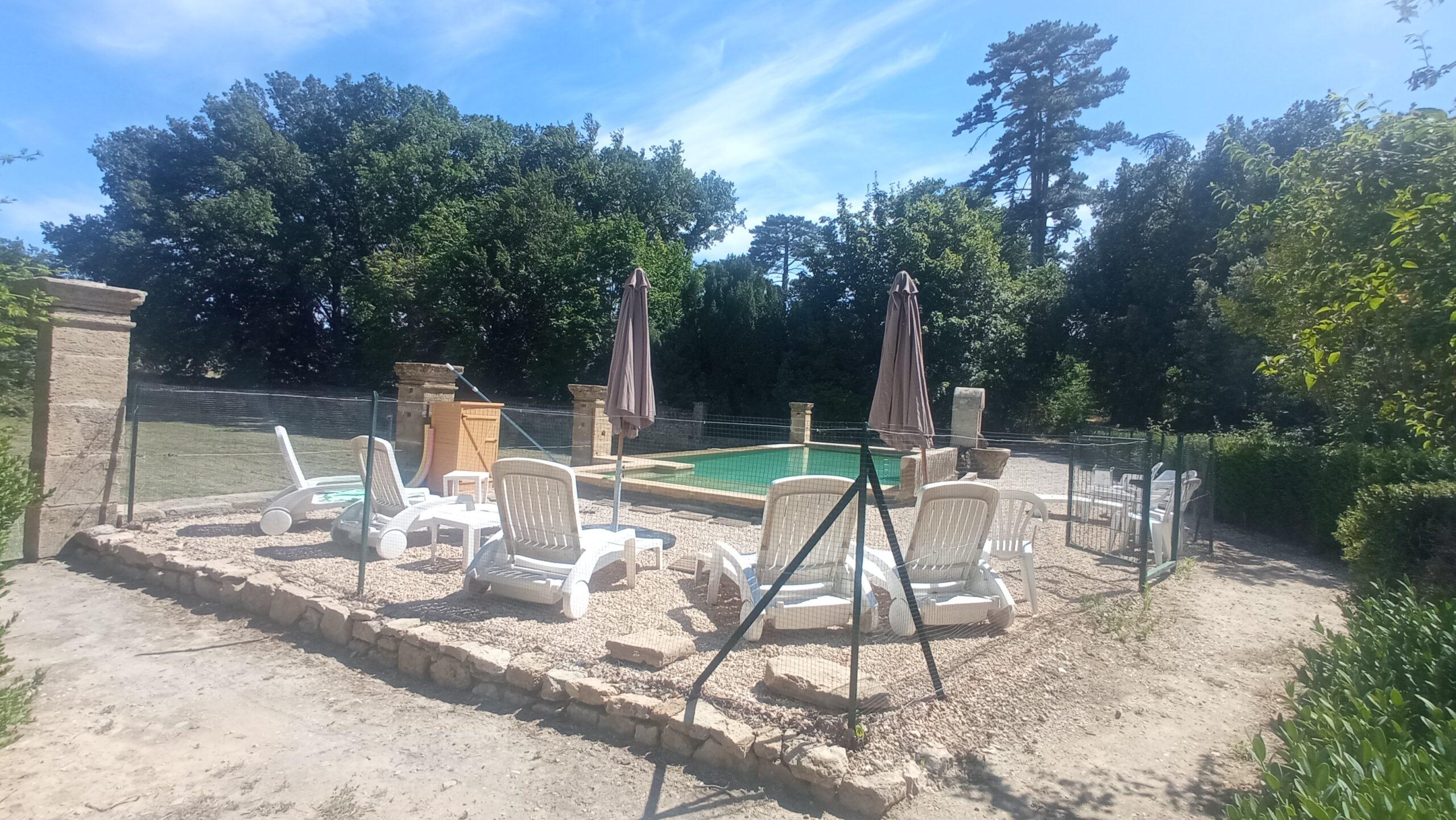 Vue de l'espace piscine sécurisée du gîte Domaine de Ribbe avec transats et parasols sous le soleil.