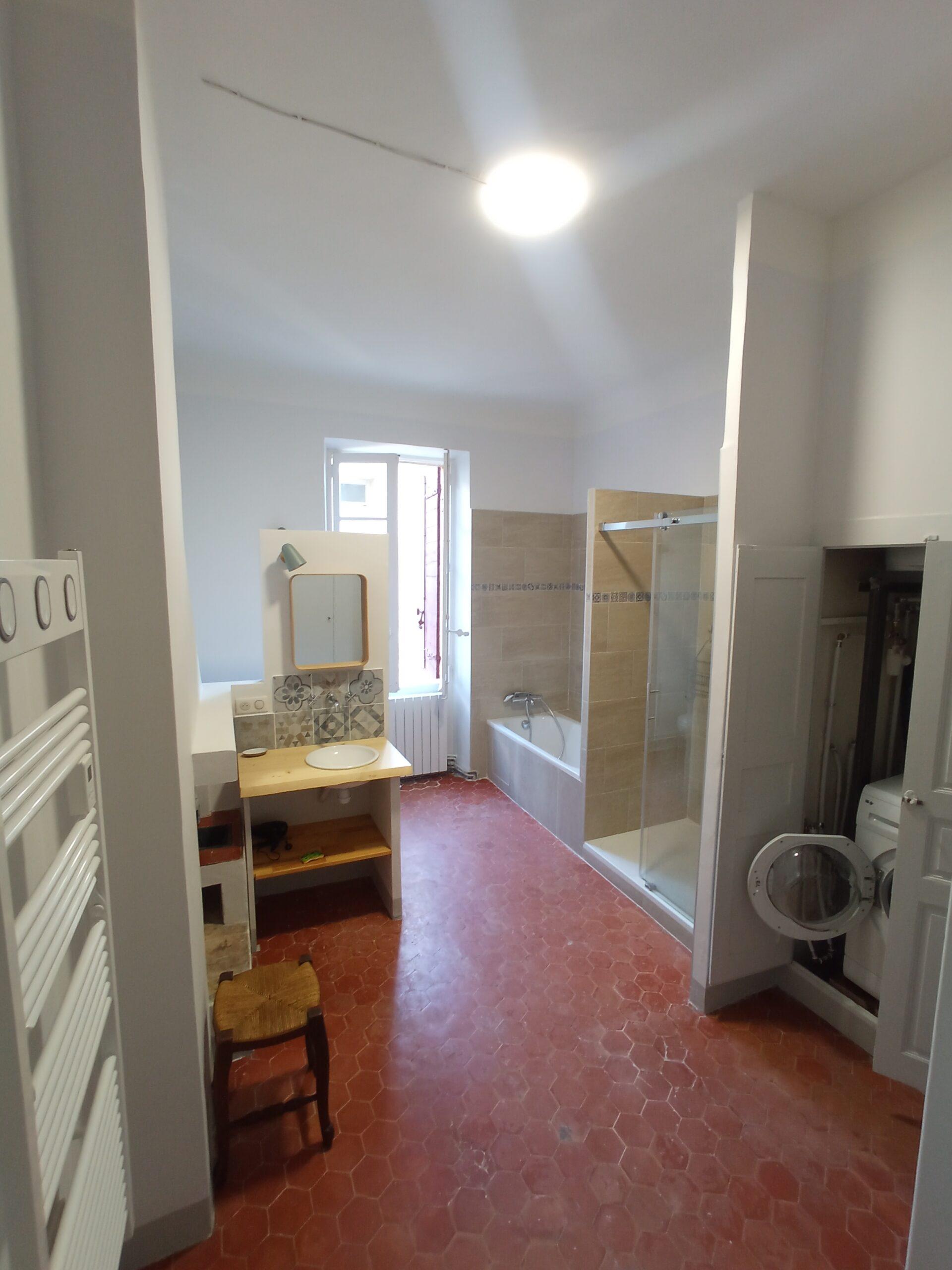 Salle de bain partagée pour les chambres 1 et 5 au Domaine de Ribbe, comprenant une baignoire, une douche, un lavabo sur meuble en bois et un lave-linge encastré, le tout sur un sol en tomettes.