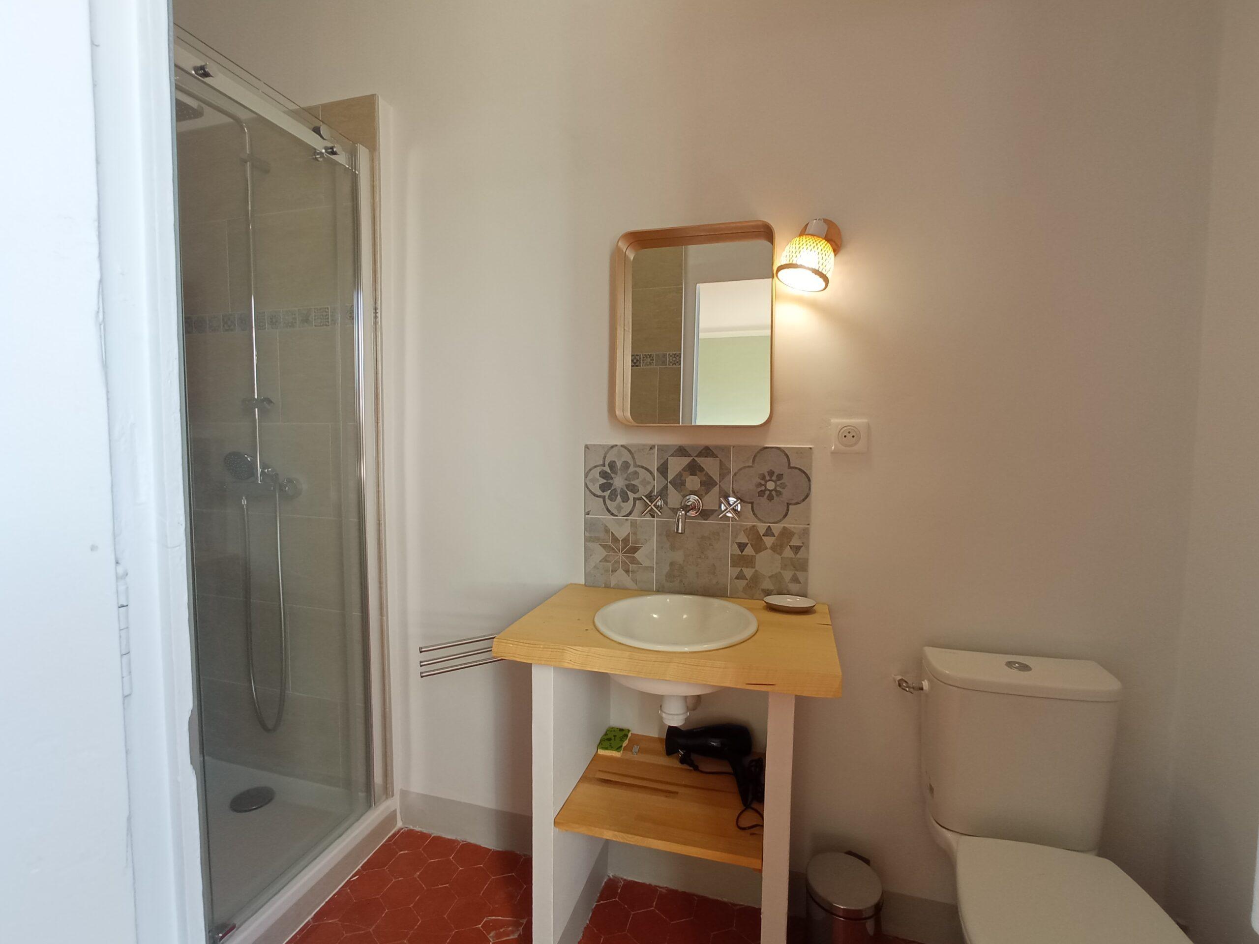 Salle de bain attenante à la chambre 2, comprenant une cabine de douche, un lavabo sur meuble en bois avec crédence en carreaux décoratifs et un WC au Domaine de Ribbe.