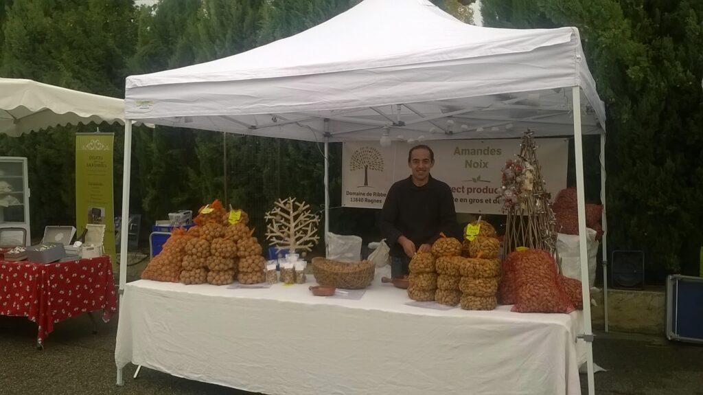 Producteur du Domaine de Ribbe sur son stand de marché vendant des noix et amandes.