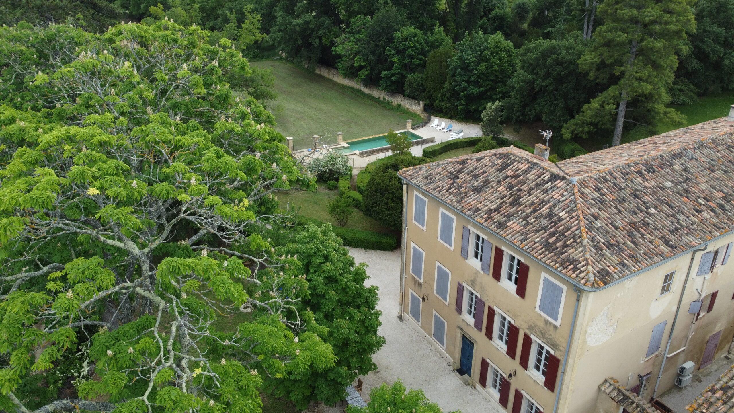 Vue aérienne en plongée du domaine de Ribbe avec la bastide, son grand marronnier en fleurs, la cour et la piscine en arrière-plan.
