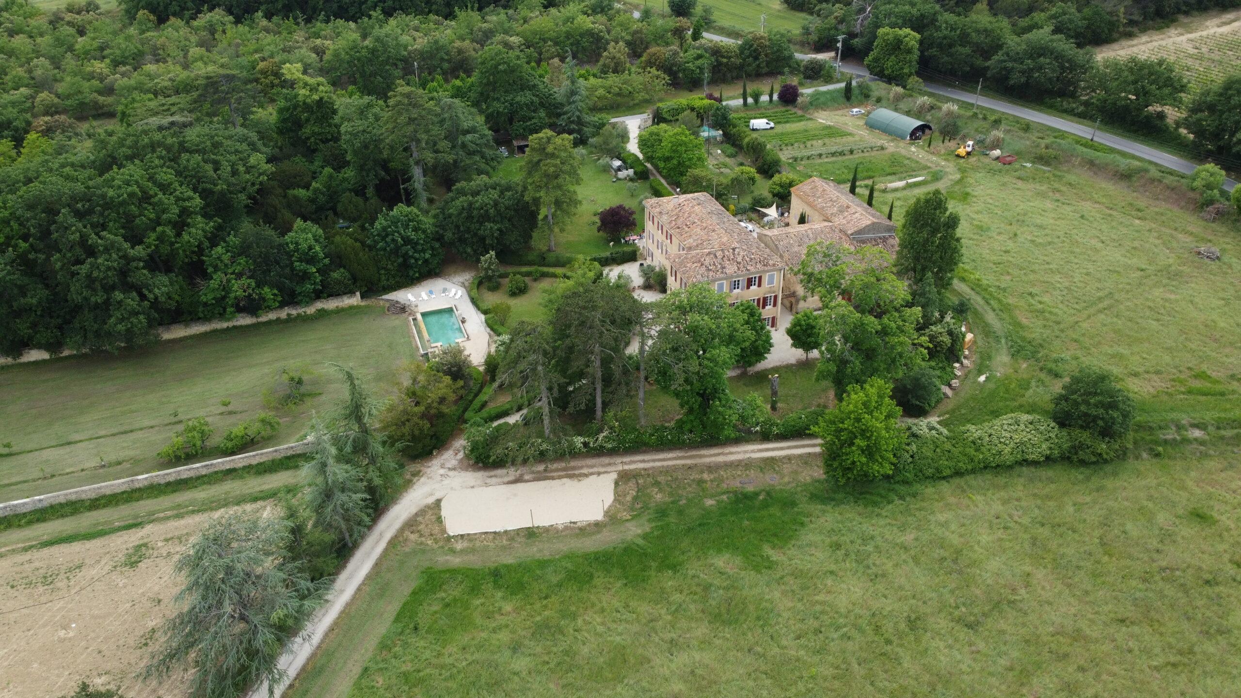 Vue aérienne grand angle de la propriété du Domaine de Ribbe montrant la bastide, la piscine, le jardin et les champs environnants.