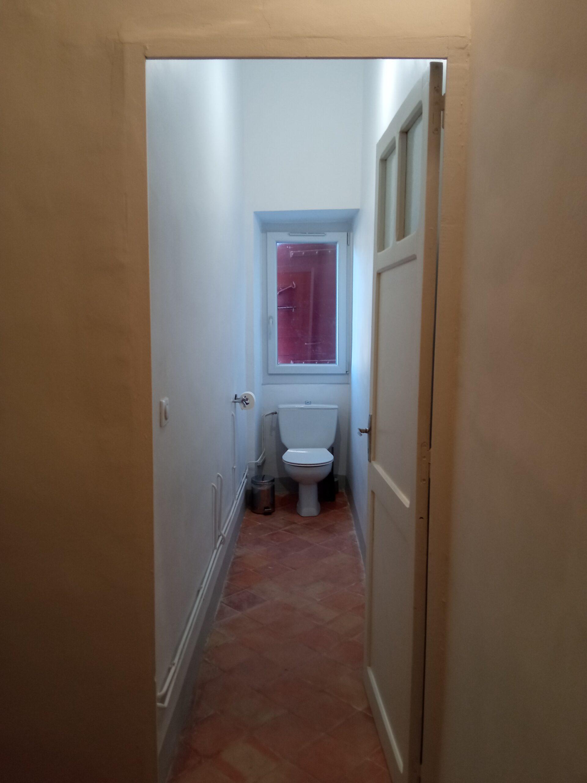 Vue intérieure des toilettes desservant les chambres 7 et 8 du Domaine de Ribbe, avec un sol en tomettes traditionnelles et une fenêtre.
